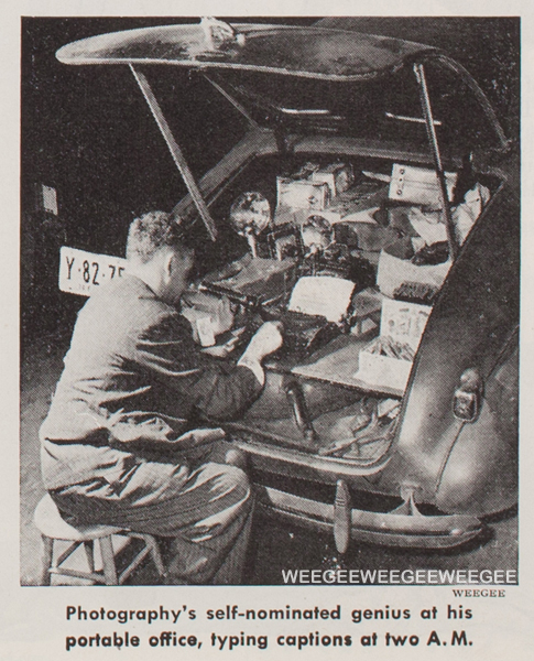 Weegee sitting behind his car typing